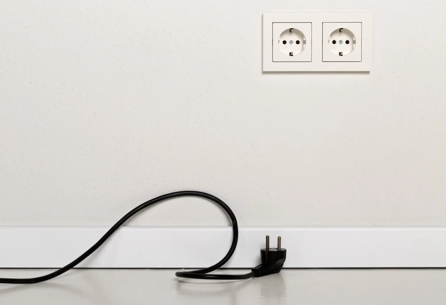 Schwarzes Netzkabel, ausgesteckt, mit europäischer Steckdose an weißer Gipswand