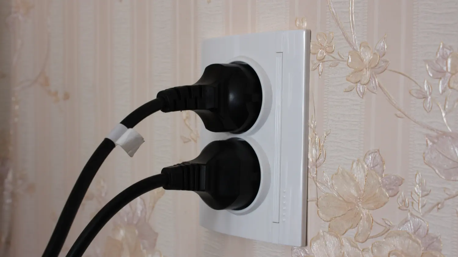 Schwarzer Stecker von einem Elektrogerät an eine weiße Steckdose. Mehrere Steckdosen mit einem schwarzen Gerätestecker.